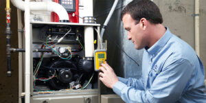 A technician in a blue shirt uses a yellow digital device to inspect the wiring inside an open HVAC unit.